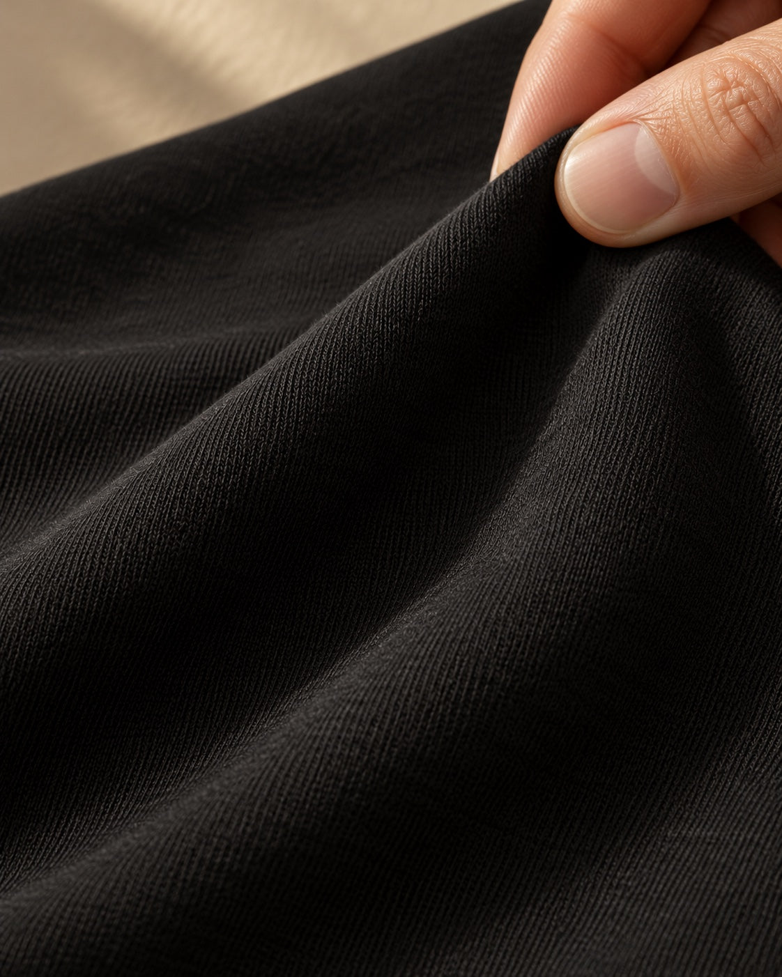 A close-up of soft black fine-knit jersey held gently between fingers.